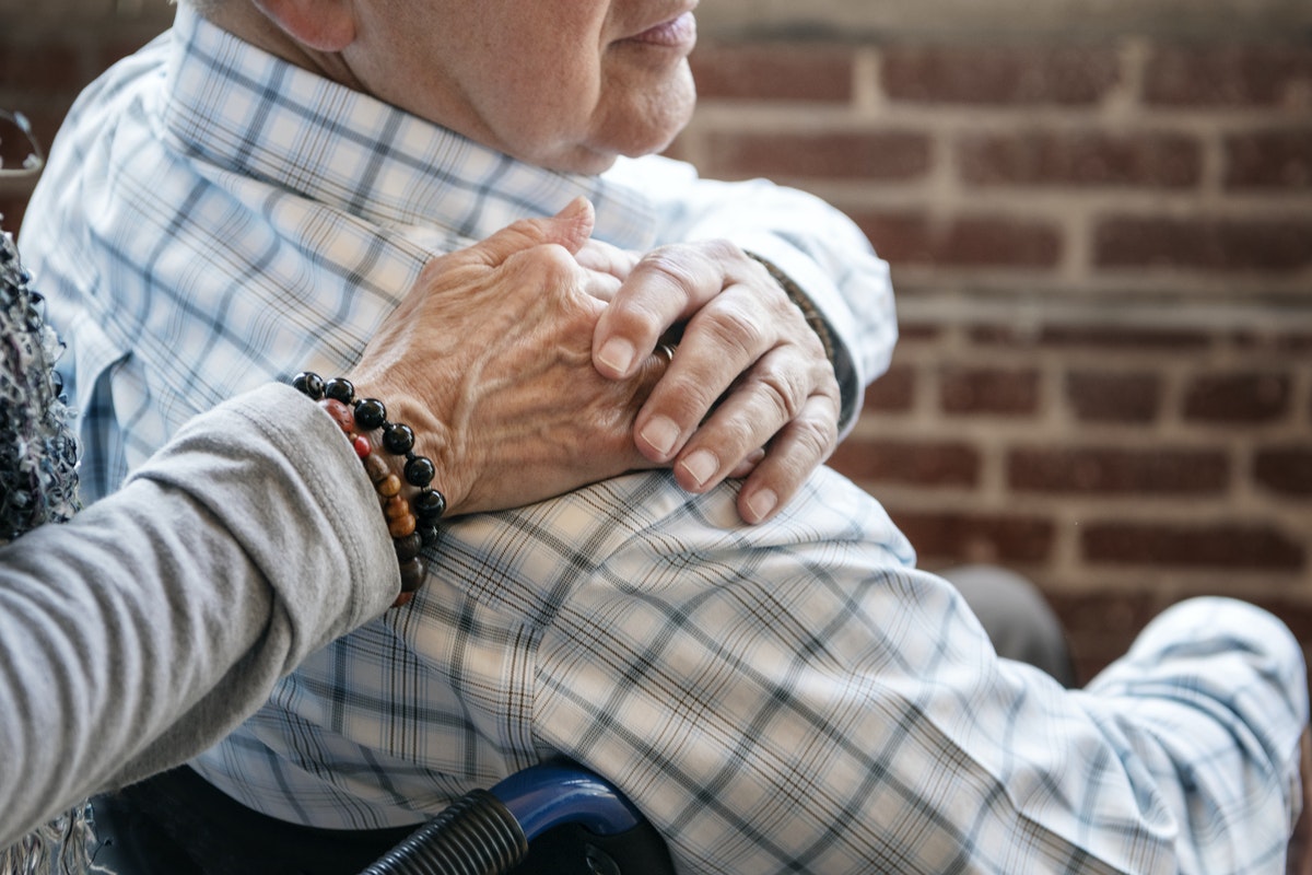 Elderly man on a wheelchair holding his wife hand on his shoulder