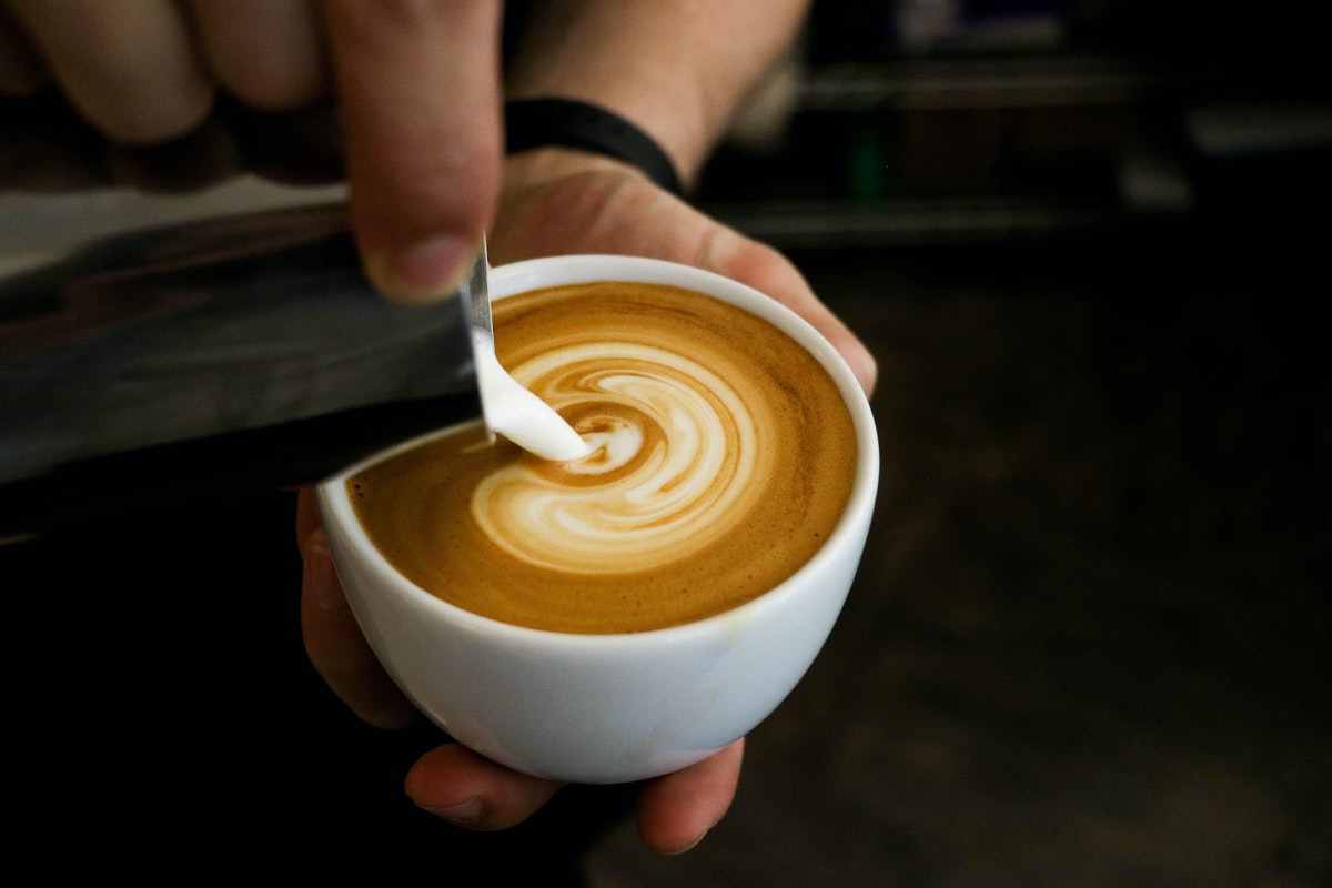 A person's hands holding a coffee cup and pouring cream into it.