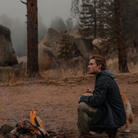 a man sitting in front of a campfire with his dog